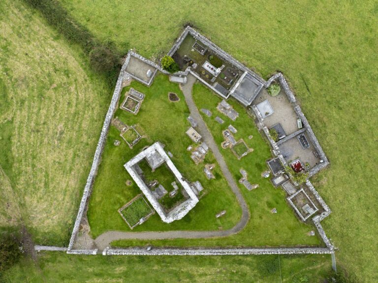 Aerial view of Killoo Church, showcasing grass grounds, masonry ruins, and surrounding stone walls and grave markers.